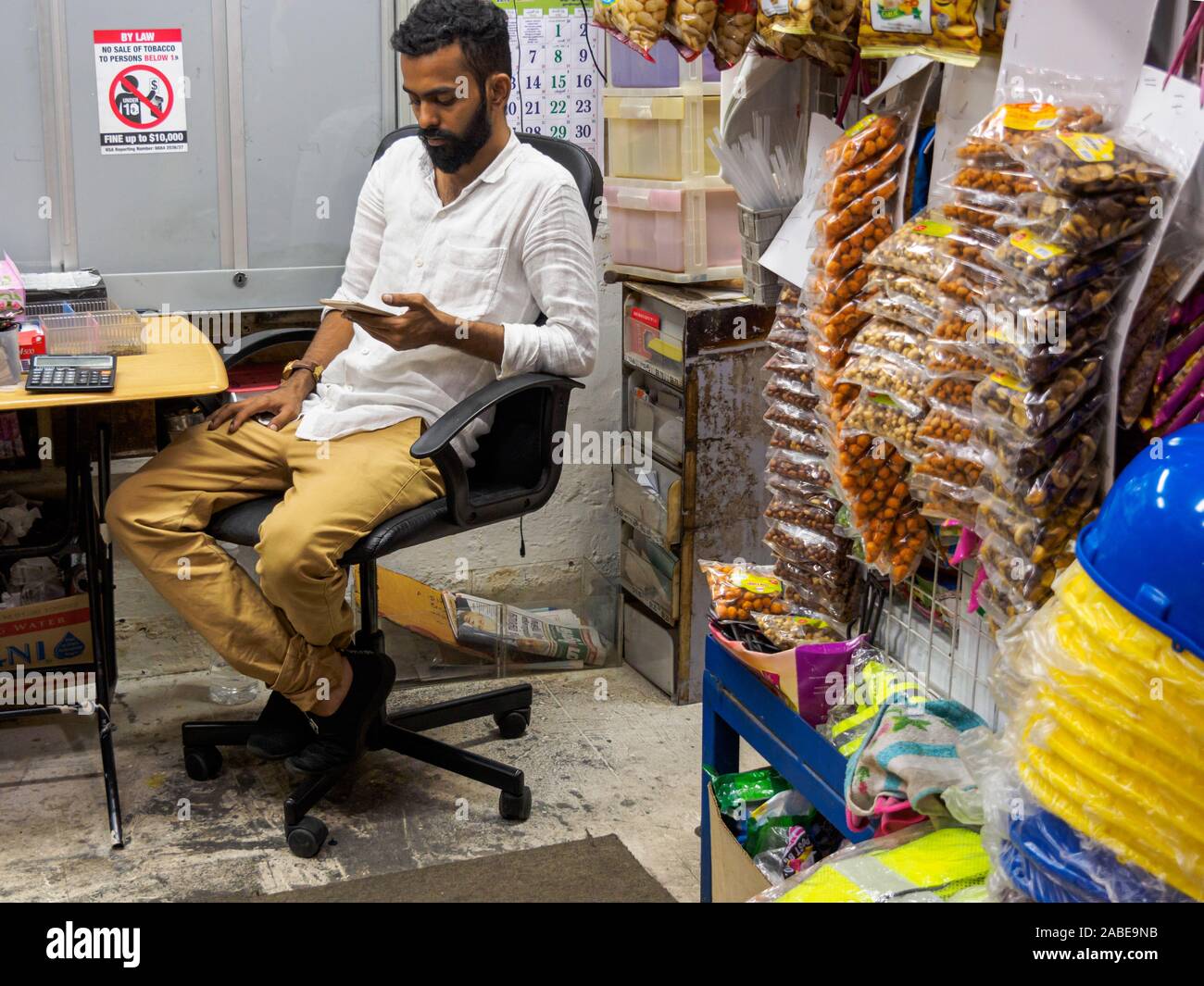 SINGAPORE - 16 MAR 2019 – A Singaporean Indian shopkeeper checks his phone in a traditional corner store / provision shop in Jalan Besar. Small busine Stock Photo