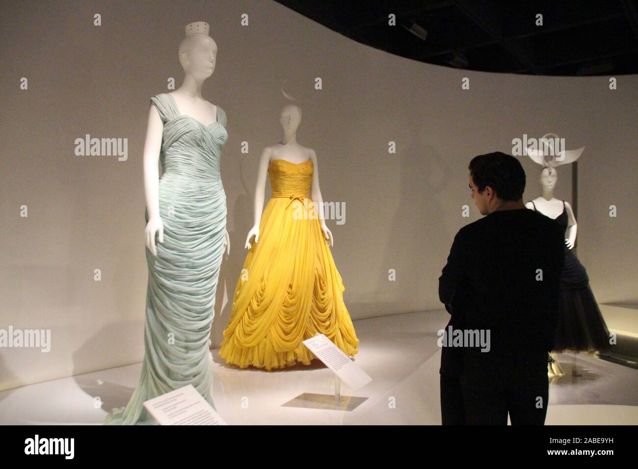 New York USA. 25th Nov 2019. A man looks at two historical designer dresses by Pierre Balmain l and Jean Desses in the exhibition In Pursuit of Fashion The Sandy Schreier Collection