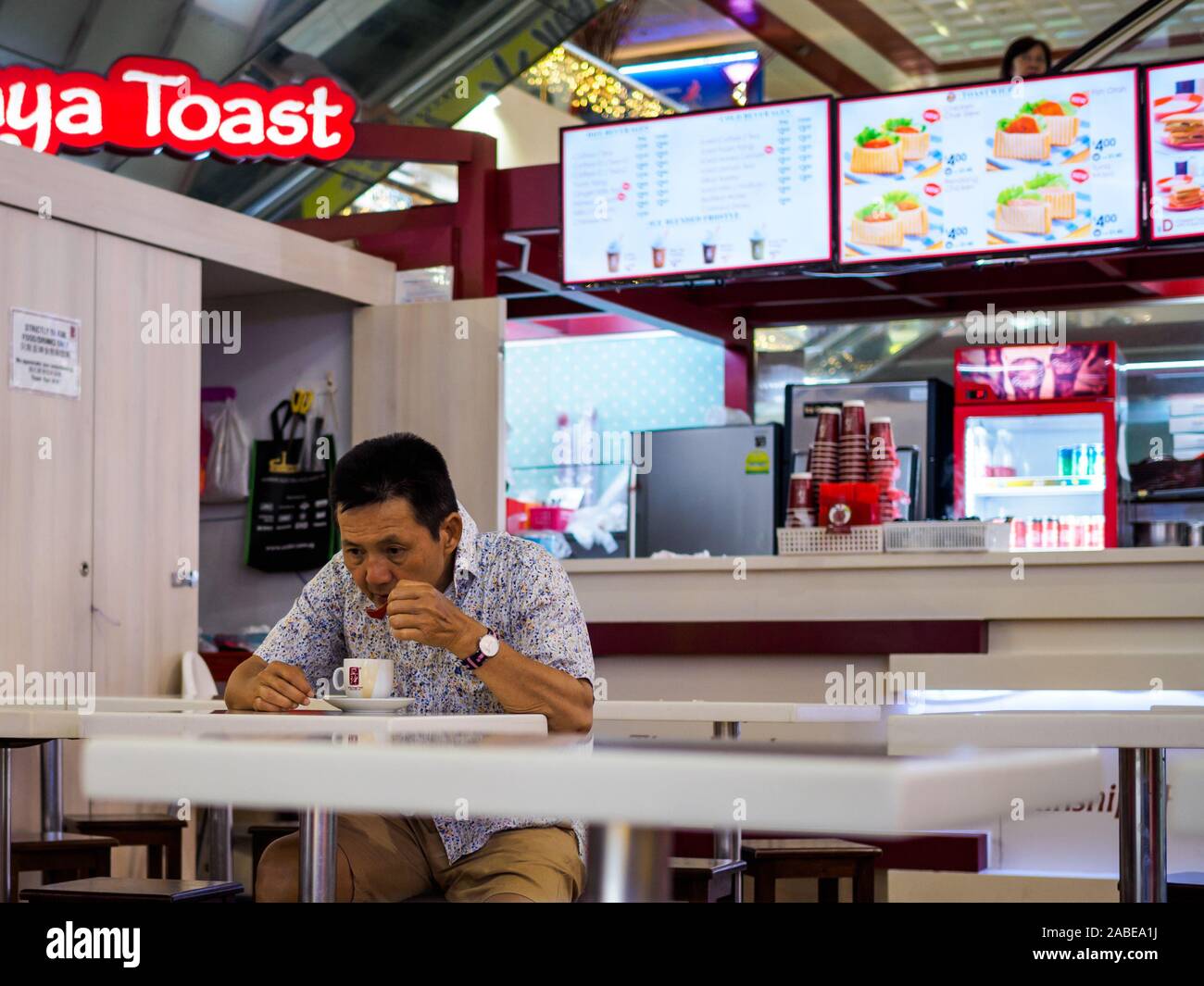 SINGAPORE – 9 MAY 2019 – Middle aged Asian Chinese Singaporean man drinks coffee with a spoon alone at a Ka Yun Kaya Toast cafe. With copy space. Stock Photo