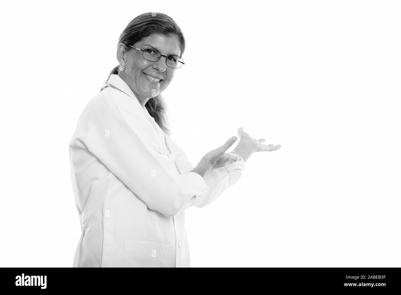 Studio shot of mature happy woman doctor smiling and showing something on the wall Stock Photo