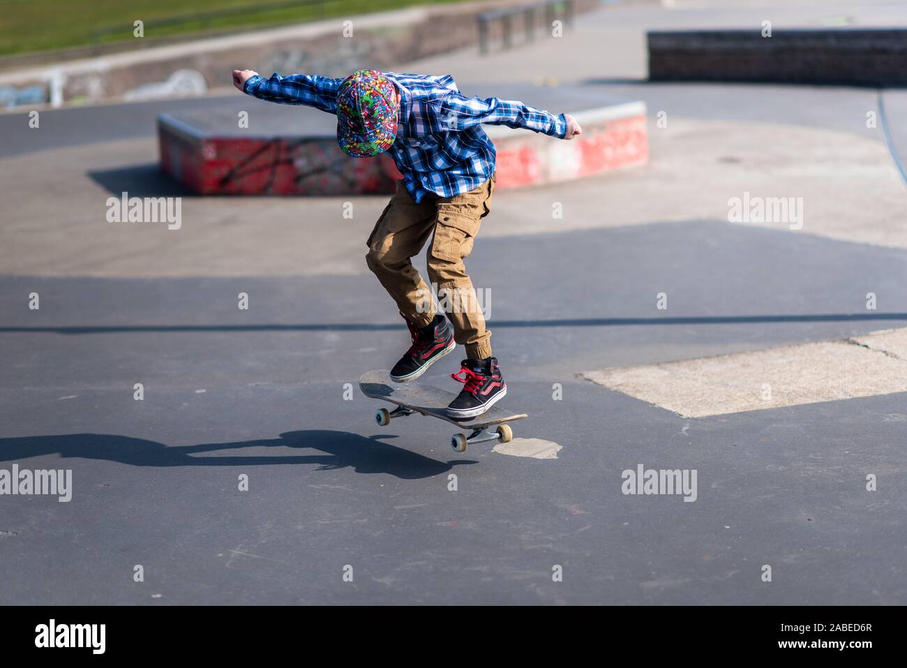 A cute little boy with ADHD, Autism, Asperger syndrome burns off energy at the Skateboard park, practicing tricks such as the ollie and jumping steps Stock Photo