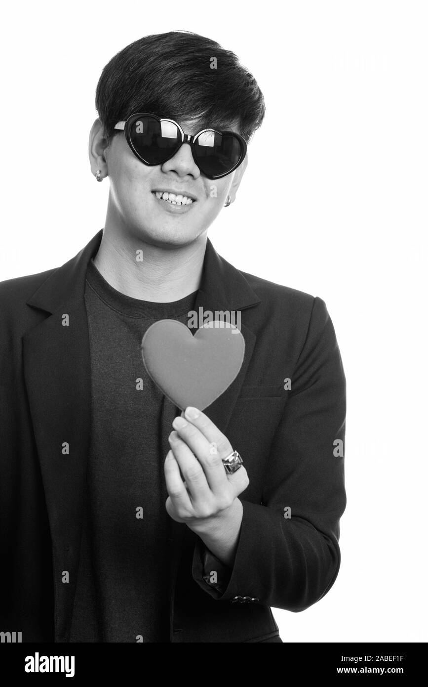 Cool happy Asian businessman smiling while wearing heart shaped sunglasses and holding red heart Stock Photo