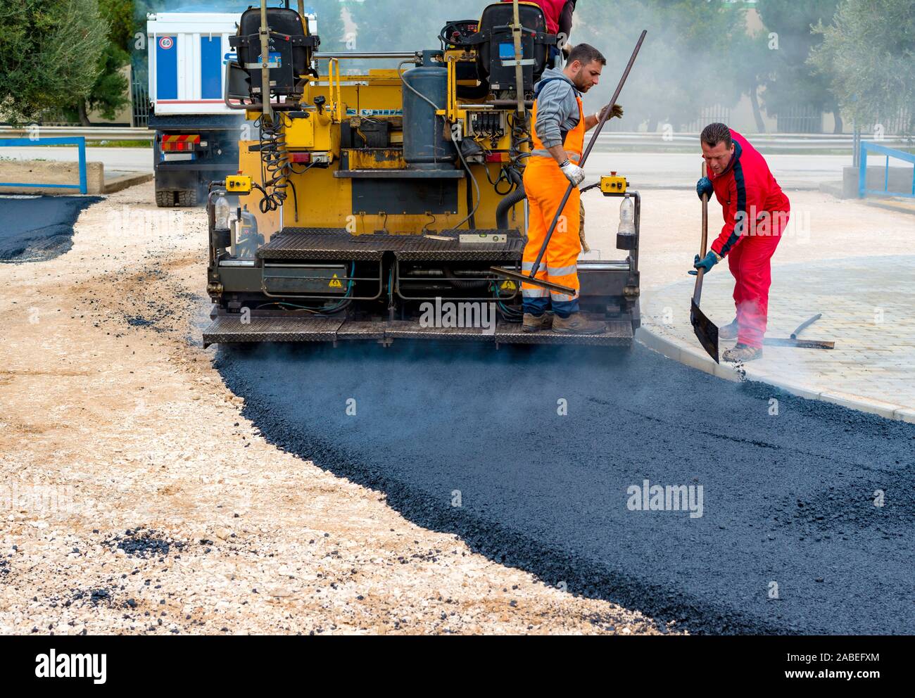 Workers regulate tracked paver laying asphalt heated to temperatures above 160 ° pavement on a runway Stock Photo