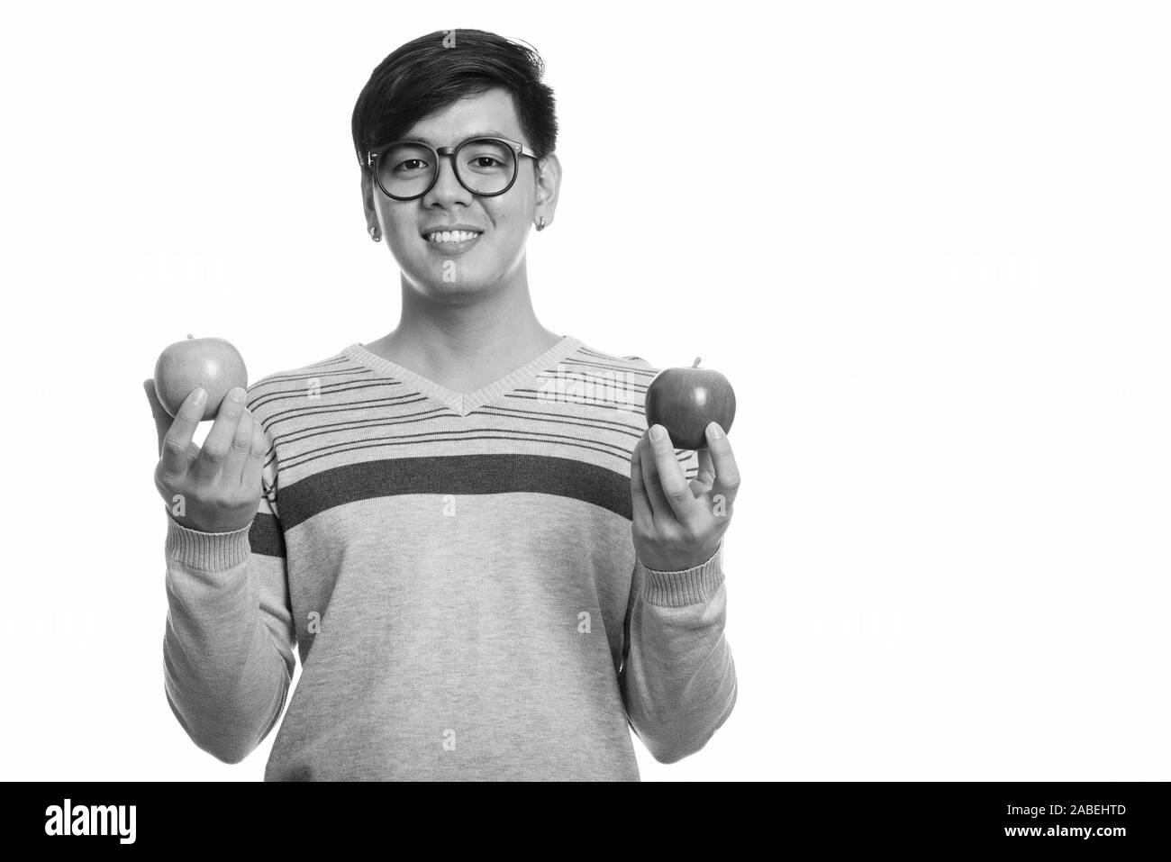 Studio shot of young happy Asian man smiling while holding red and ...