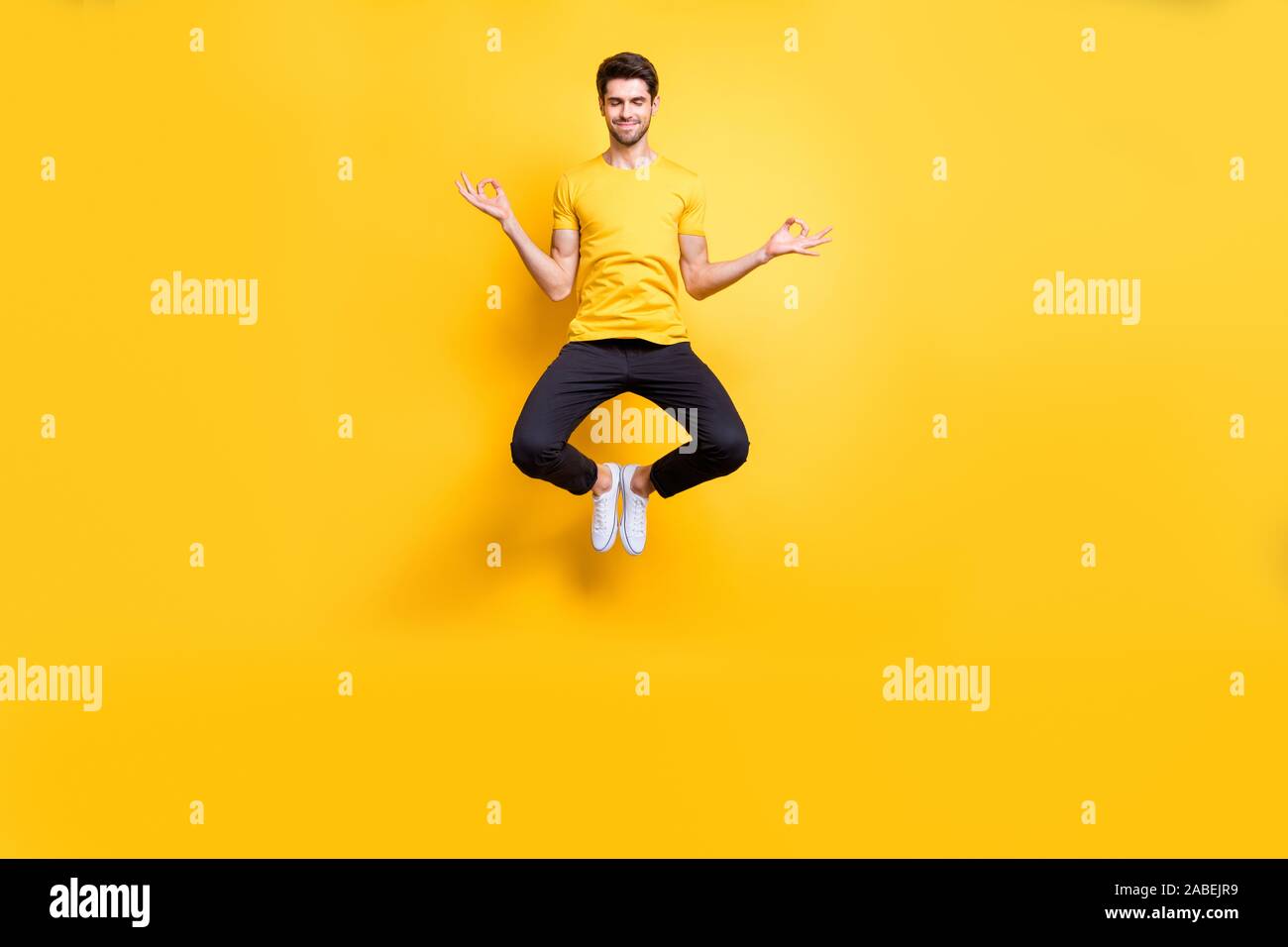 Full body photo of handsome guy jumping high lotus position morning yoga training relaxing fingers together wear casual t-shirt black trousers Stock Photo