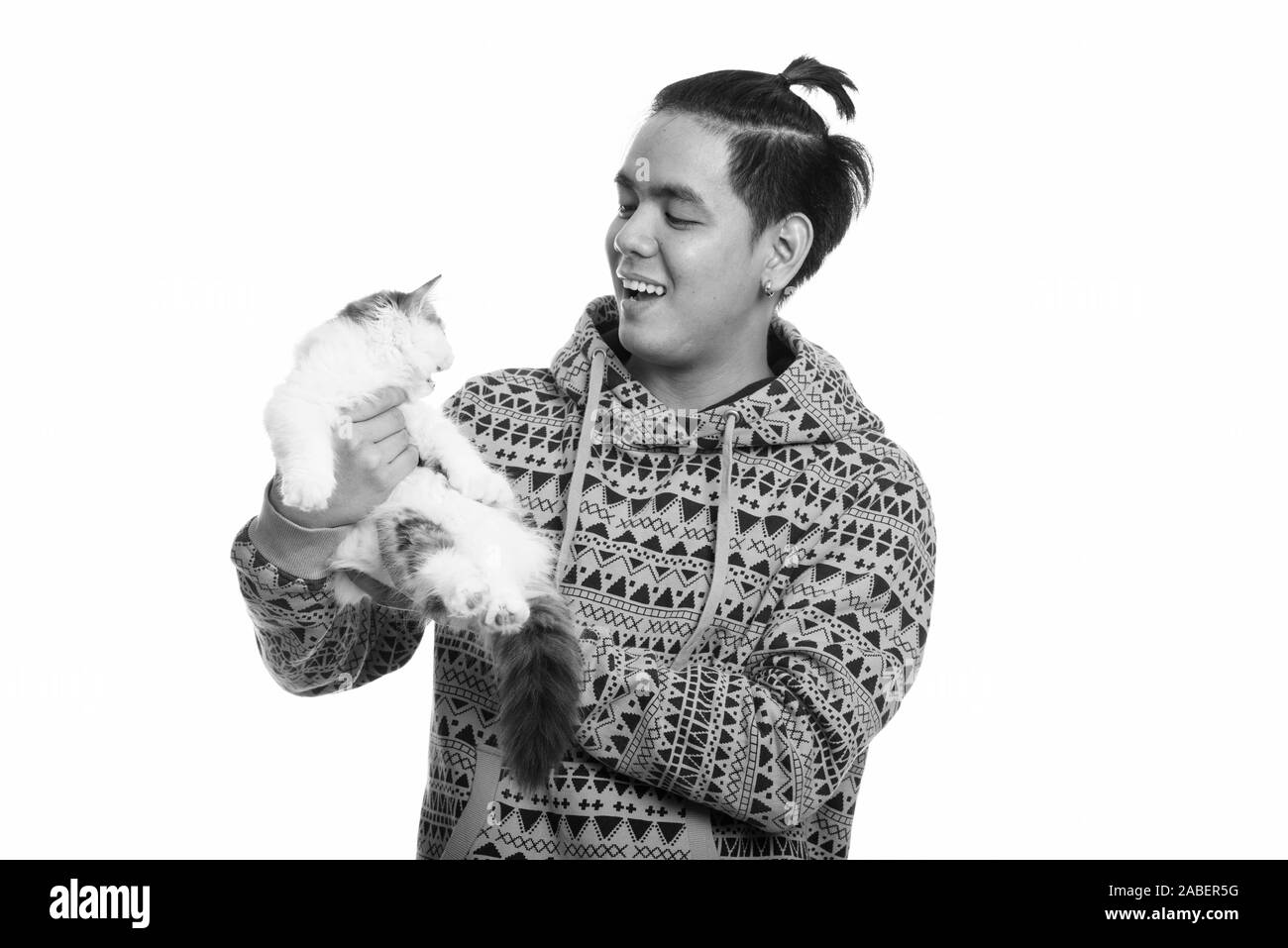 Studio shot of young happy Asian man smiling while holding cute cat Stock Photo