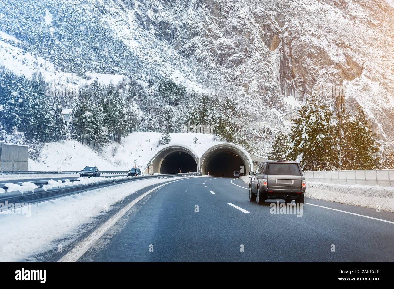 Winter alpine road landscape with tunnel, forest, mountains and blue sky on background at bright cold sunny day. Car trip family travel journey Stock Photo