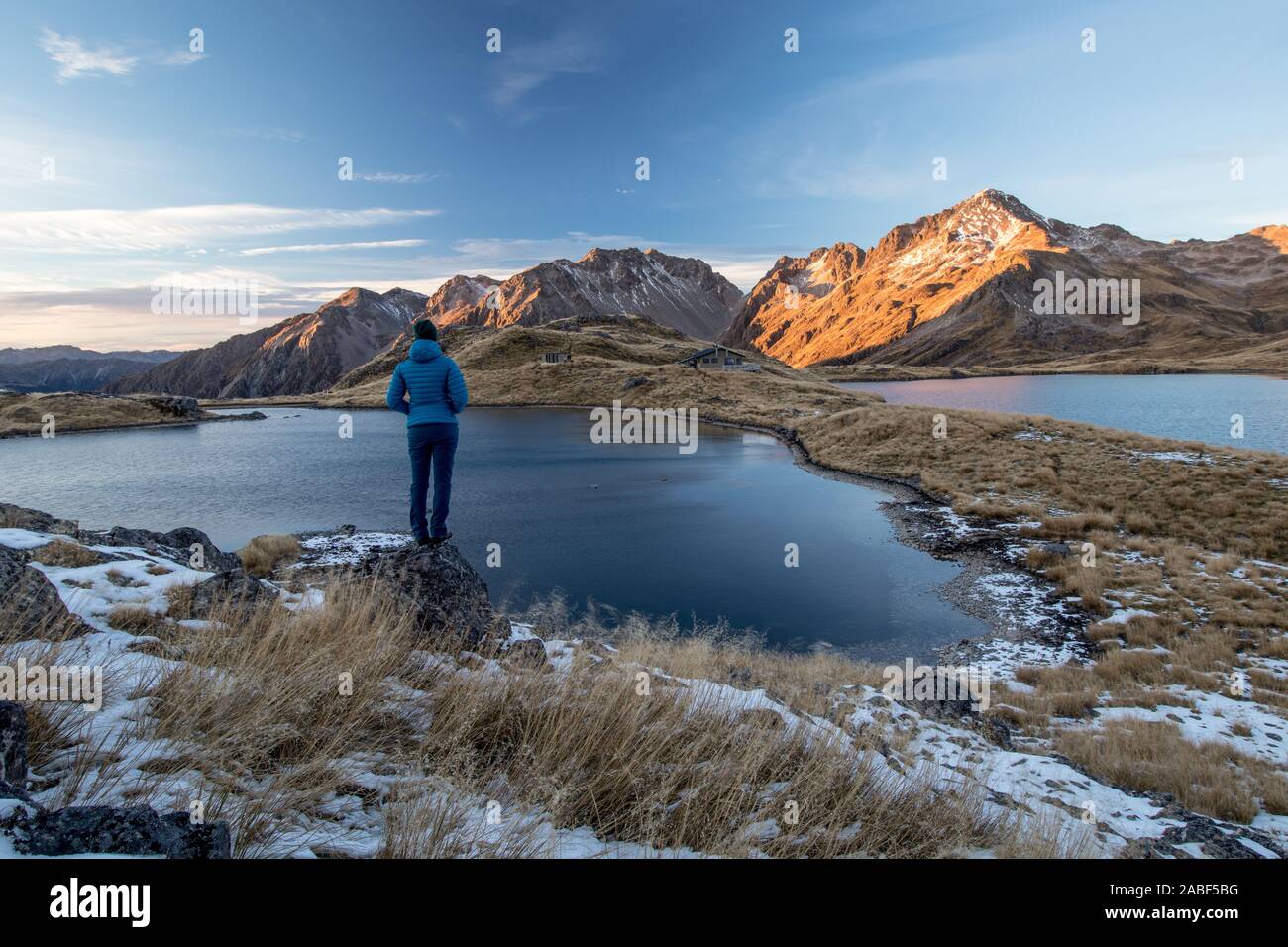 View on Angelus Lakes and winter mountain scene during sunset with sporty young woman standing on a rock facing backwards. Nelson Lakes National Park, Stock Photo