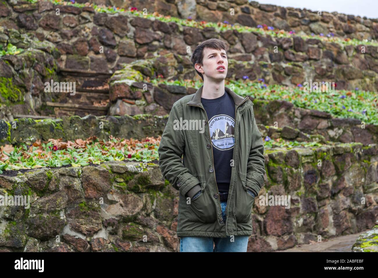 A handsome young man in his late teens or early twenties stands outdoors and looks into the distance with a worried or concerned expression. Stock Photo