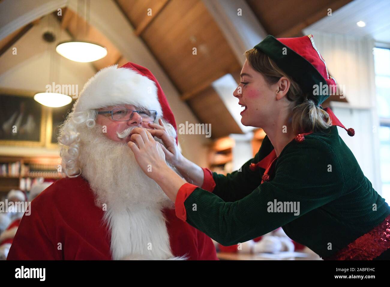 An elf adjusts a Father Christmas performer's moustache in a classroom during the 23rd annual Santa School at Southwark Cathedral in London. Stock Photo
