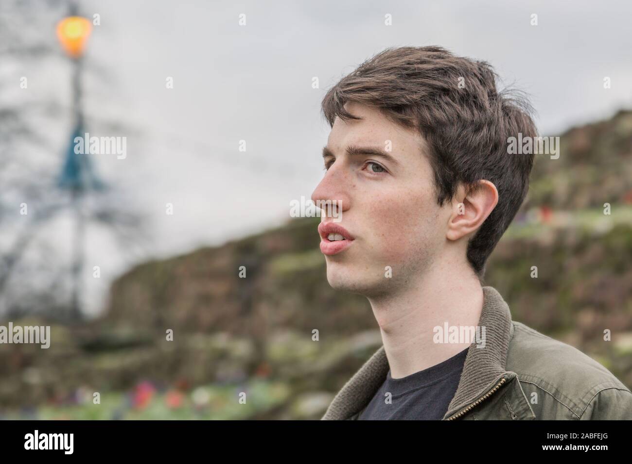 A young man in his late teens or early twenties stands outdoors with a pensive expression as he looks into the distance. Stock Photo