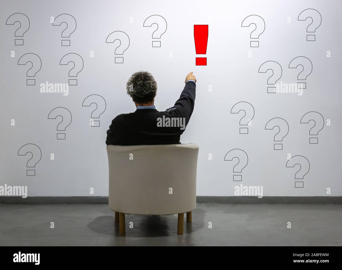 a man points to an exclamation point among many question marks. concept of idea, certainty, solution Stock Photo