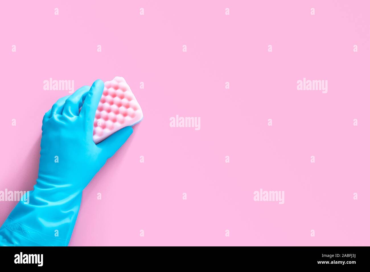 hand in blue rubber glove holding pink cleaning sponge isolated on pink background with copy space for text or logo Stock Photo