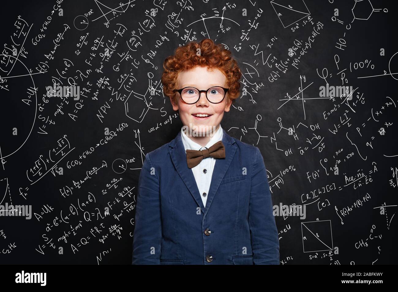 Cute redhead child in school uniform on blackboard background with science formulas Stock Photo