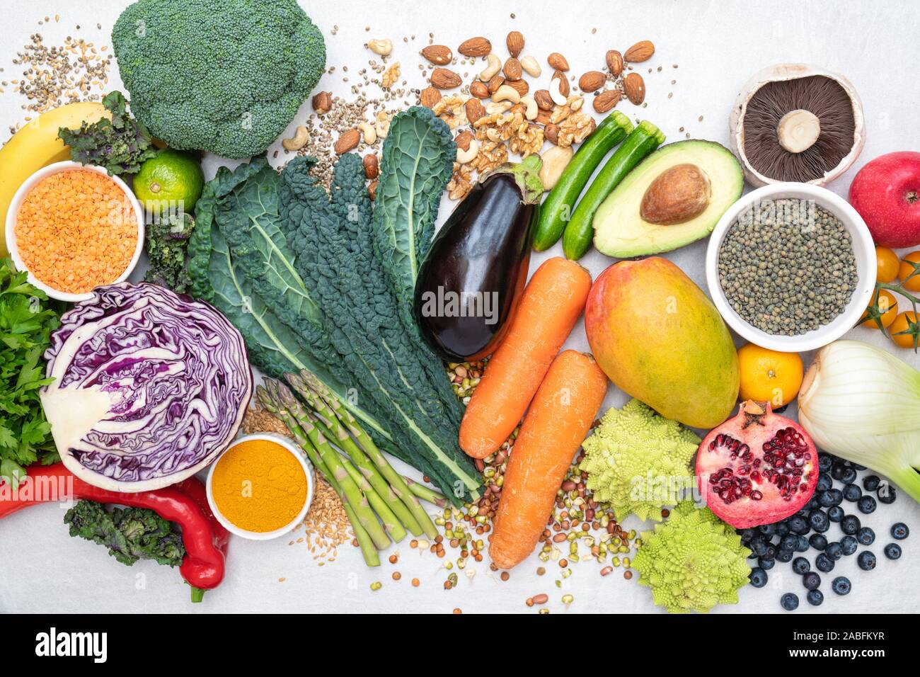 Vegan. Fruit vegetables lentils spices herbs nuts and seeds on a white slate background Stock Photo