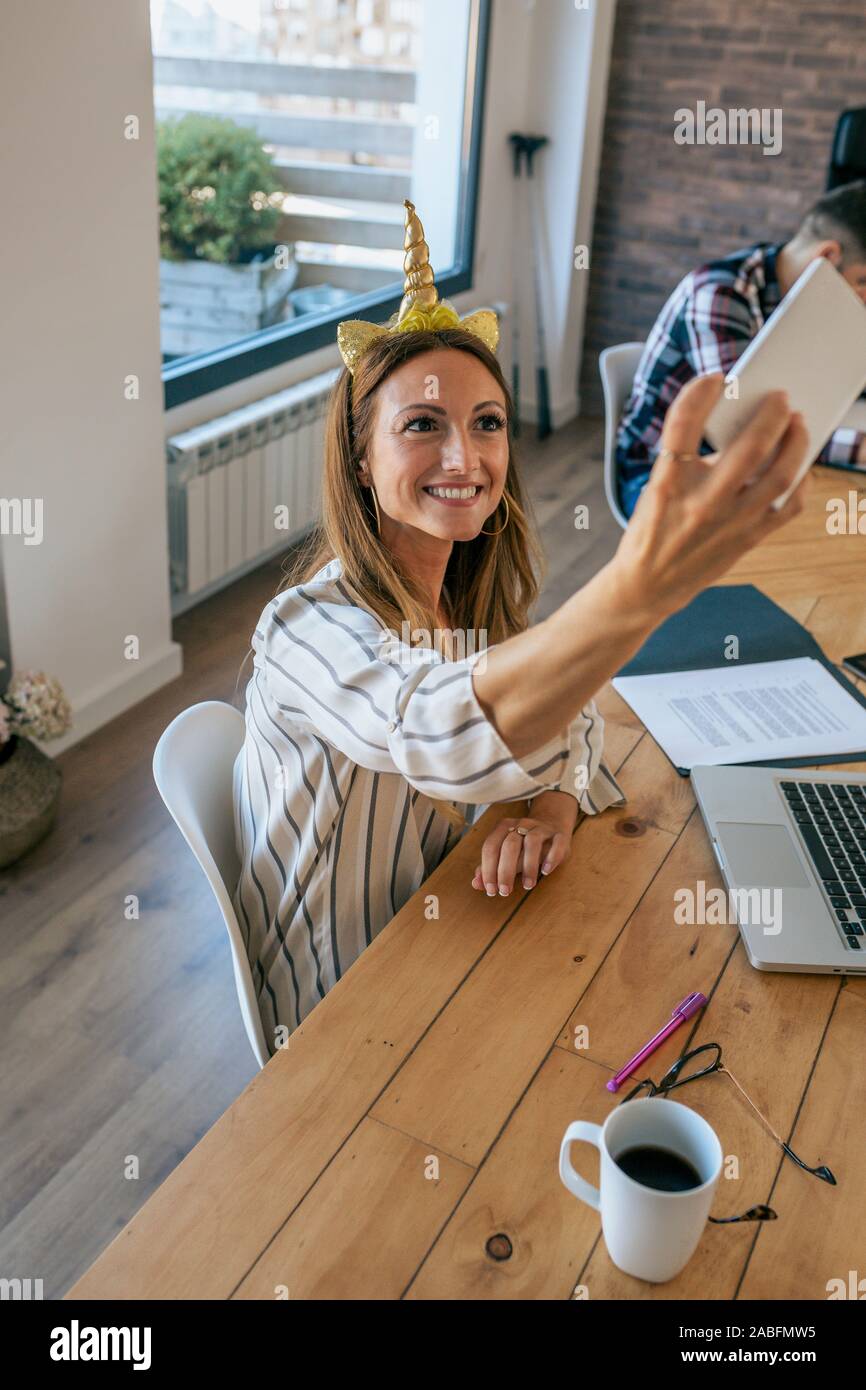 Businesswoman taking selfie with unicorn headband Stock Photo