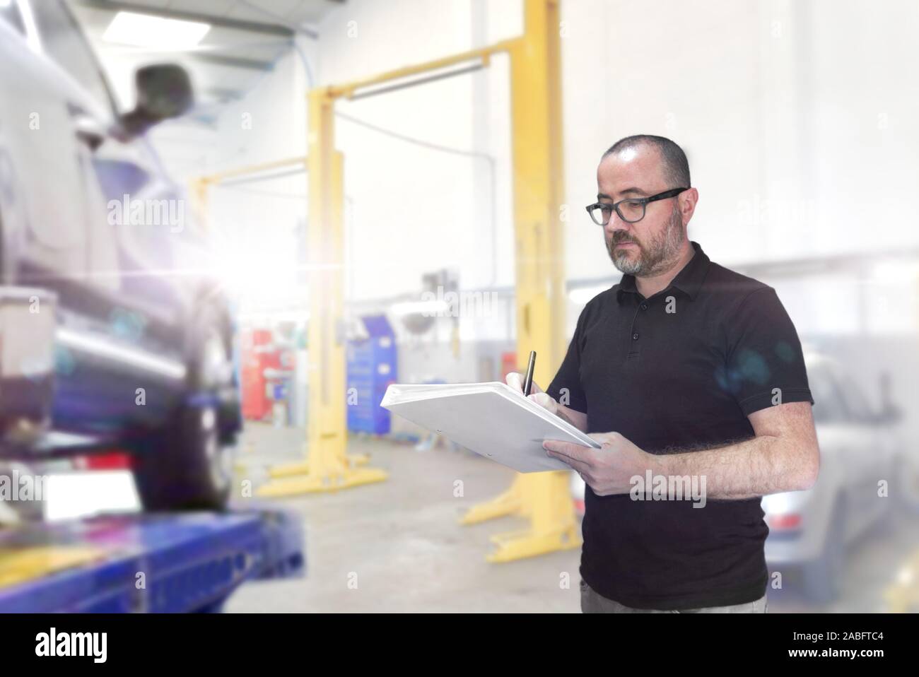 Young man with a check list for a car revision. Repair workshop with empty copy space for Editor's text. Stock Photo
