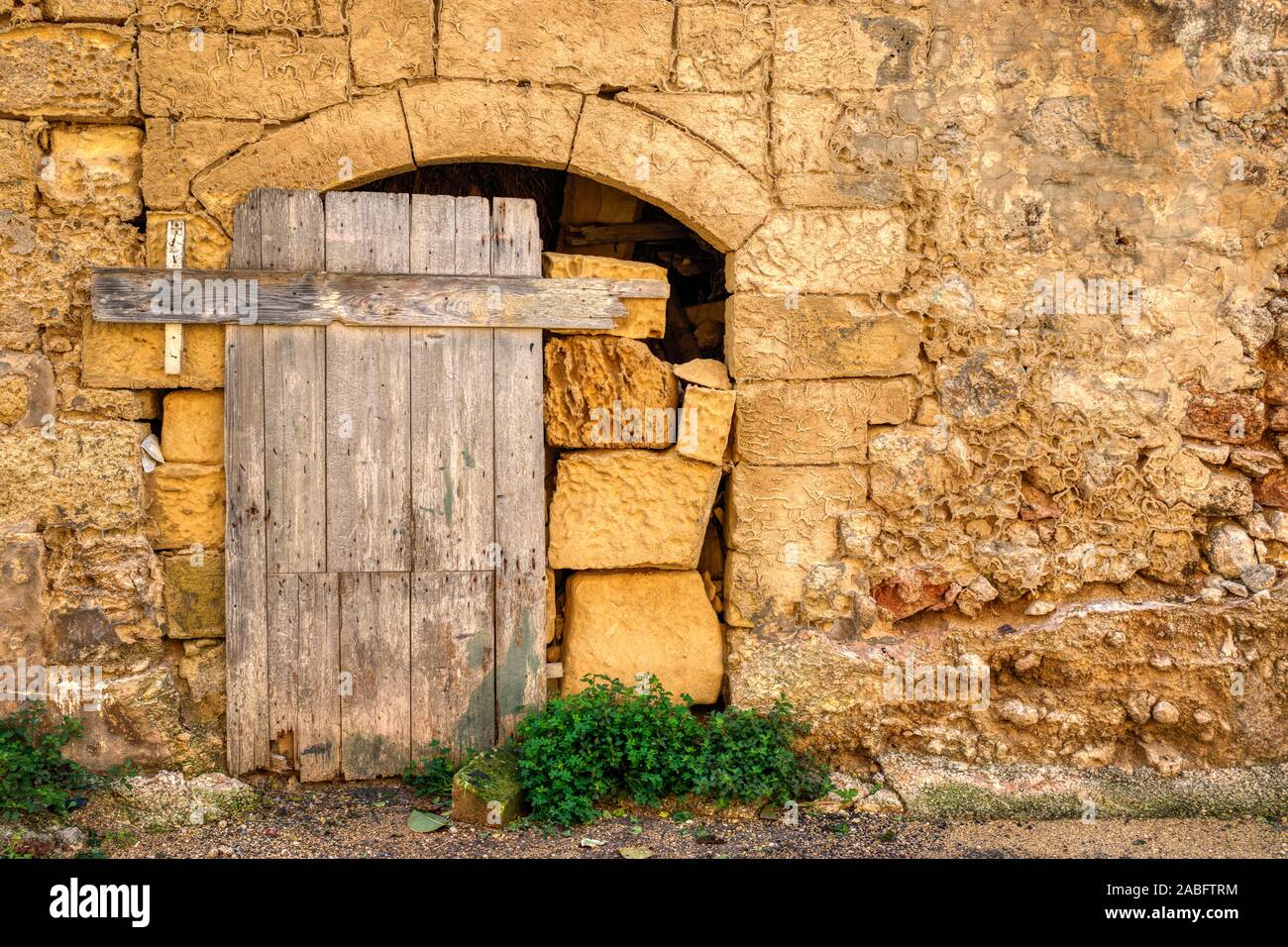 Traditional weathered and aged limestone block wall with wooden doorway. Part of a building on the Mediterranean island of Gozo, Malta. Stock Photo