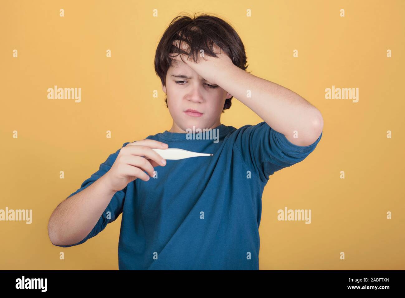 diseased child with a thermomether, measuring his fever on yellow background Stock Photo