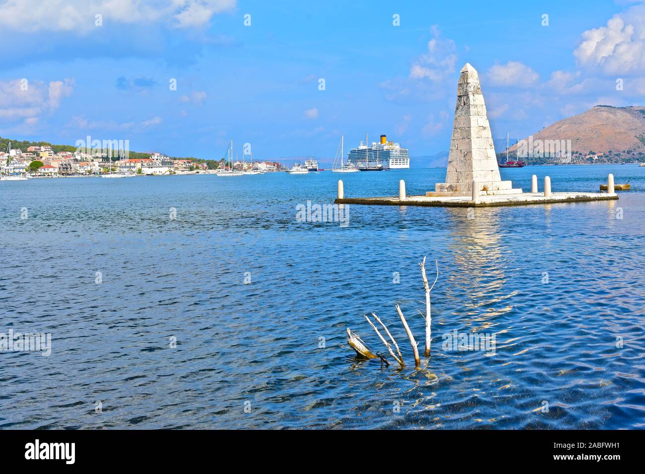 The Kolona obelisk dating from 1813, viewed from De Bosset Bridge, with Argostoli town waterfront in the background. Cruise liner moored at terminal. Stock Photo