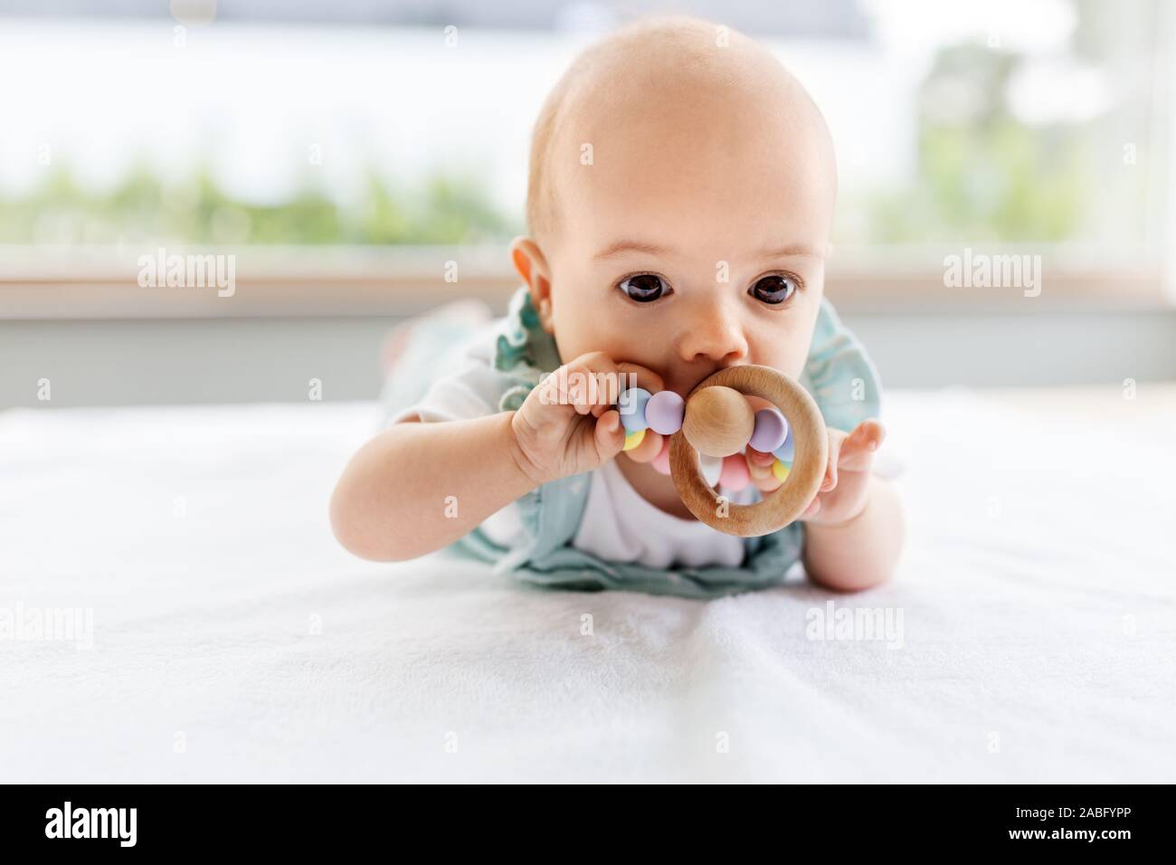 baby girl on white blanket chewing wooden rattle Stock Photo Alamy