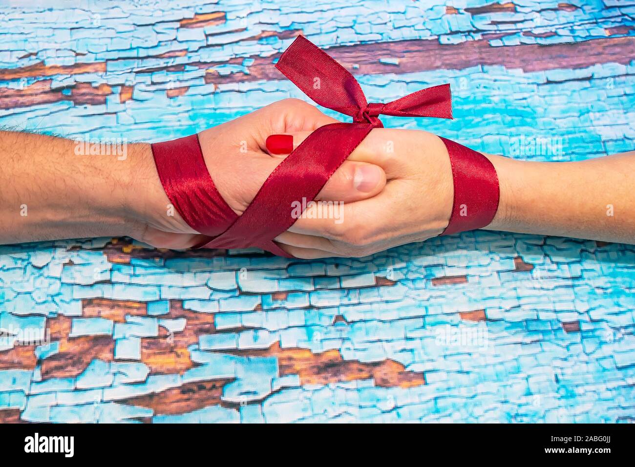 A red ribbon binds two hands, one of a woman and the other of a man on a blue and brown background Stock Photo