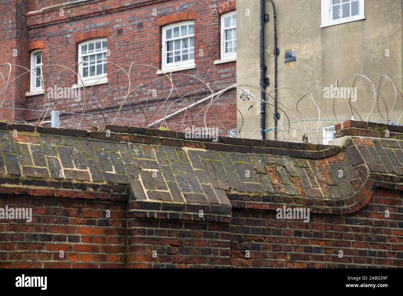 Tall and high brick wall with barbed / razor wire on the top of it, for ...