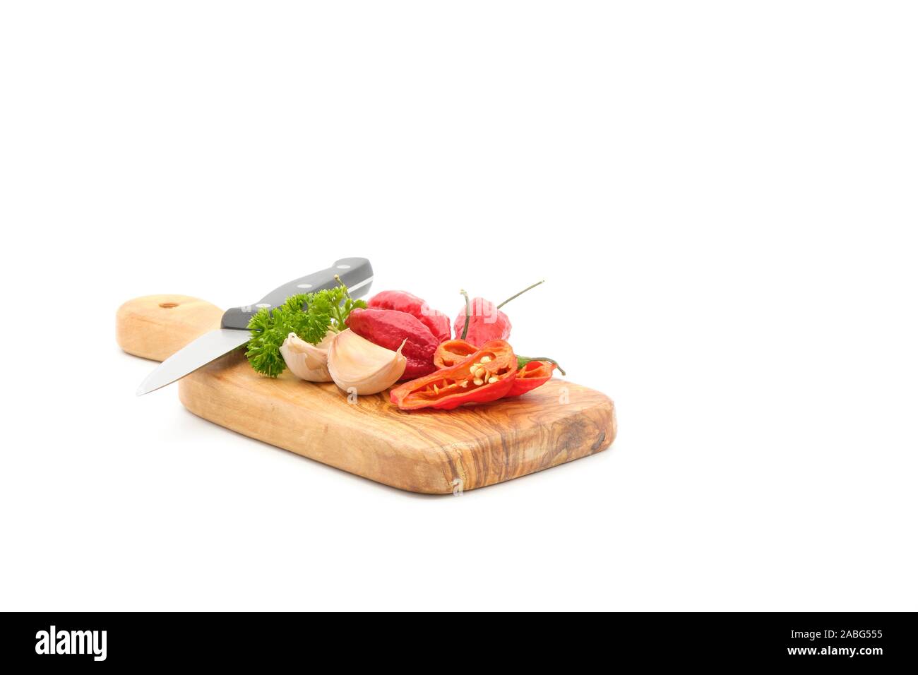 Several ingredients required for making homemade chili including red chilis, garlic and parsley lay on a wooden cutting board photographed on a white Stock Photo