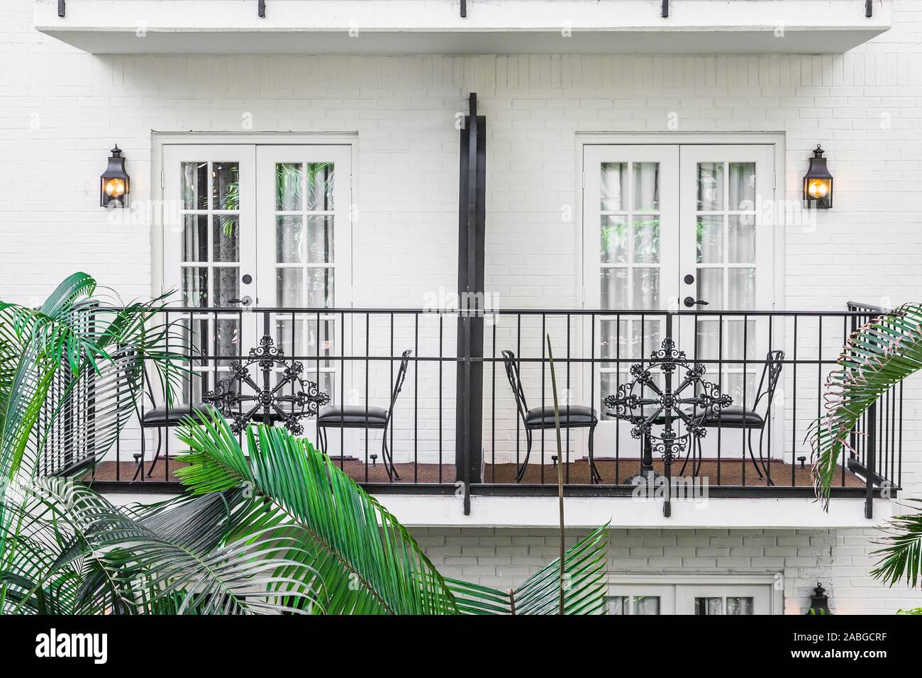 A set of balconies on a white building with tables and chairs sitting in front of the doors and trees outside. Stock Photo