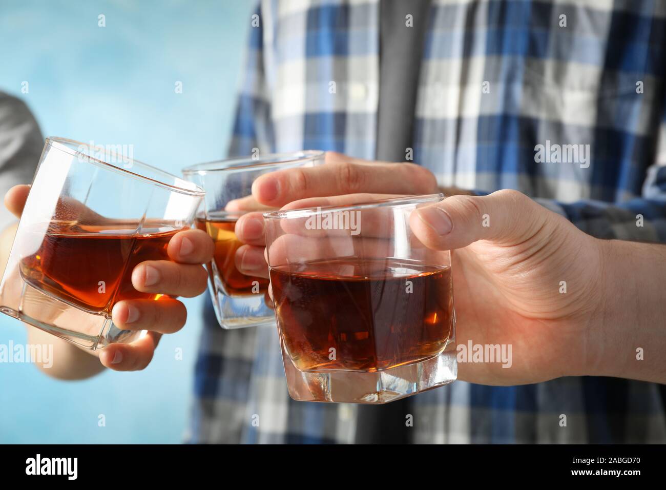 Men drink, cheers. Glasses of whiskey against blue background, close up Stock Photo