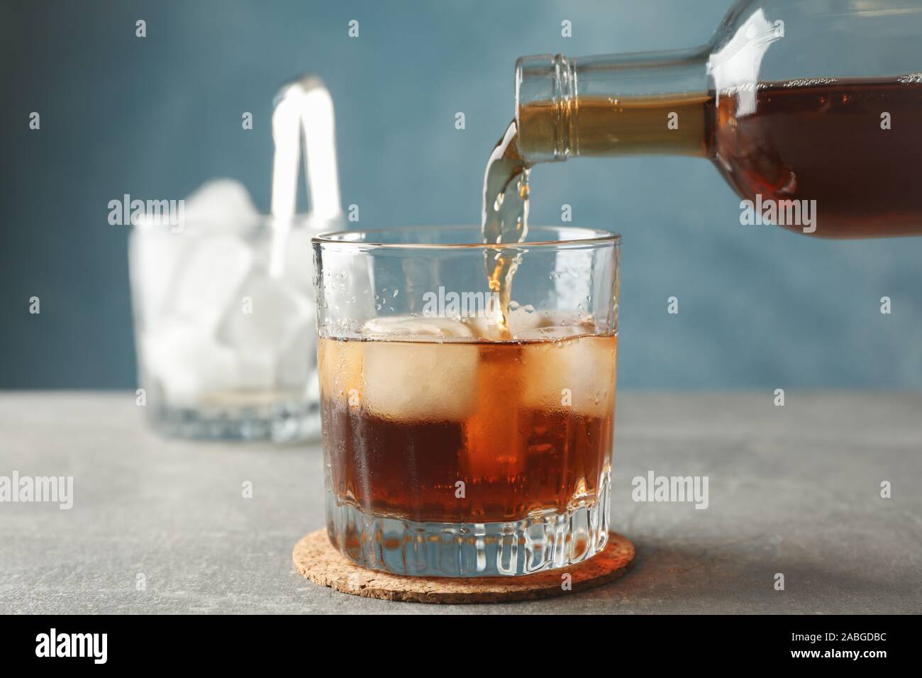 Bottle, glass of whiskey and ice cubes on grey background, close up Stock Photo