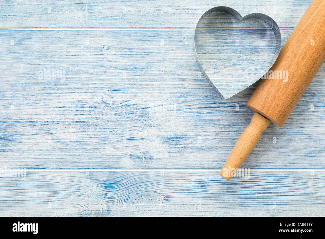 Rolling pin and heart shaped cookie cutter on blue wooden background with copy space Stock Photo