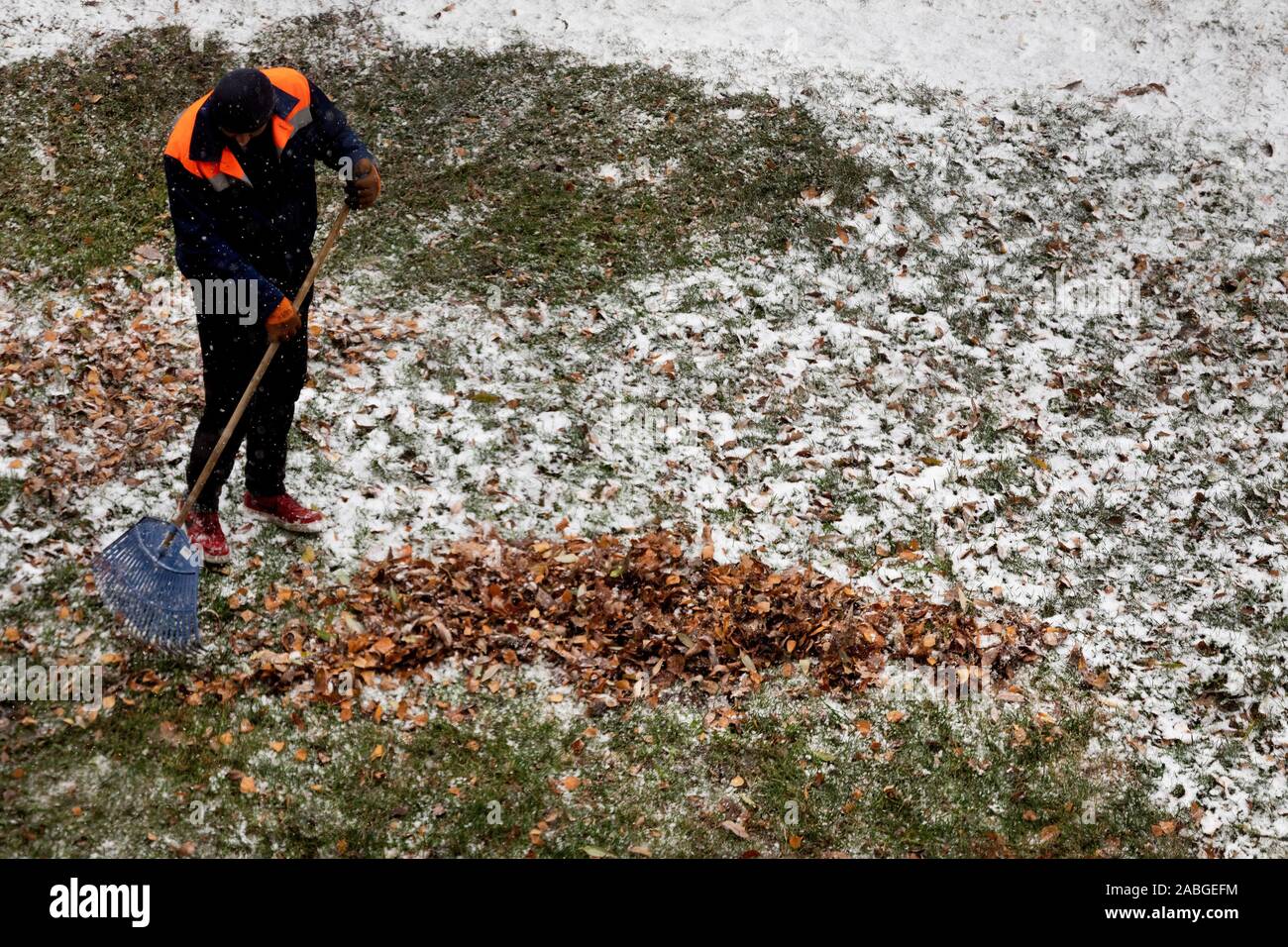 A utility worker removes fallen leaves from lawns in the local area in Moscow during the first snowfall, Russia Stock Photo