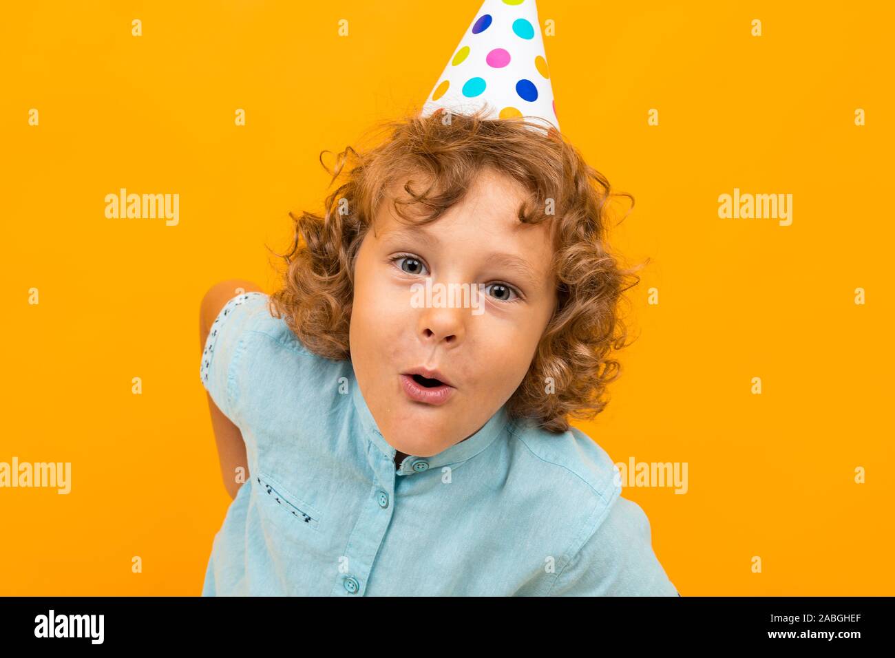 European red-haired curly boy with a festive cap is grimacing at the camera on a yellow background Stock Photo