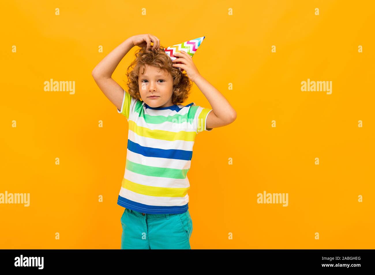 Attractive curly red-haired boy with a festive cap on a yellow background Stock Photo