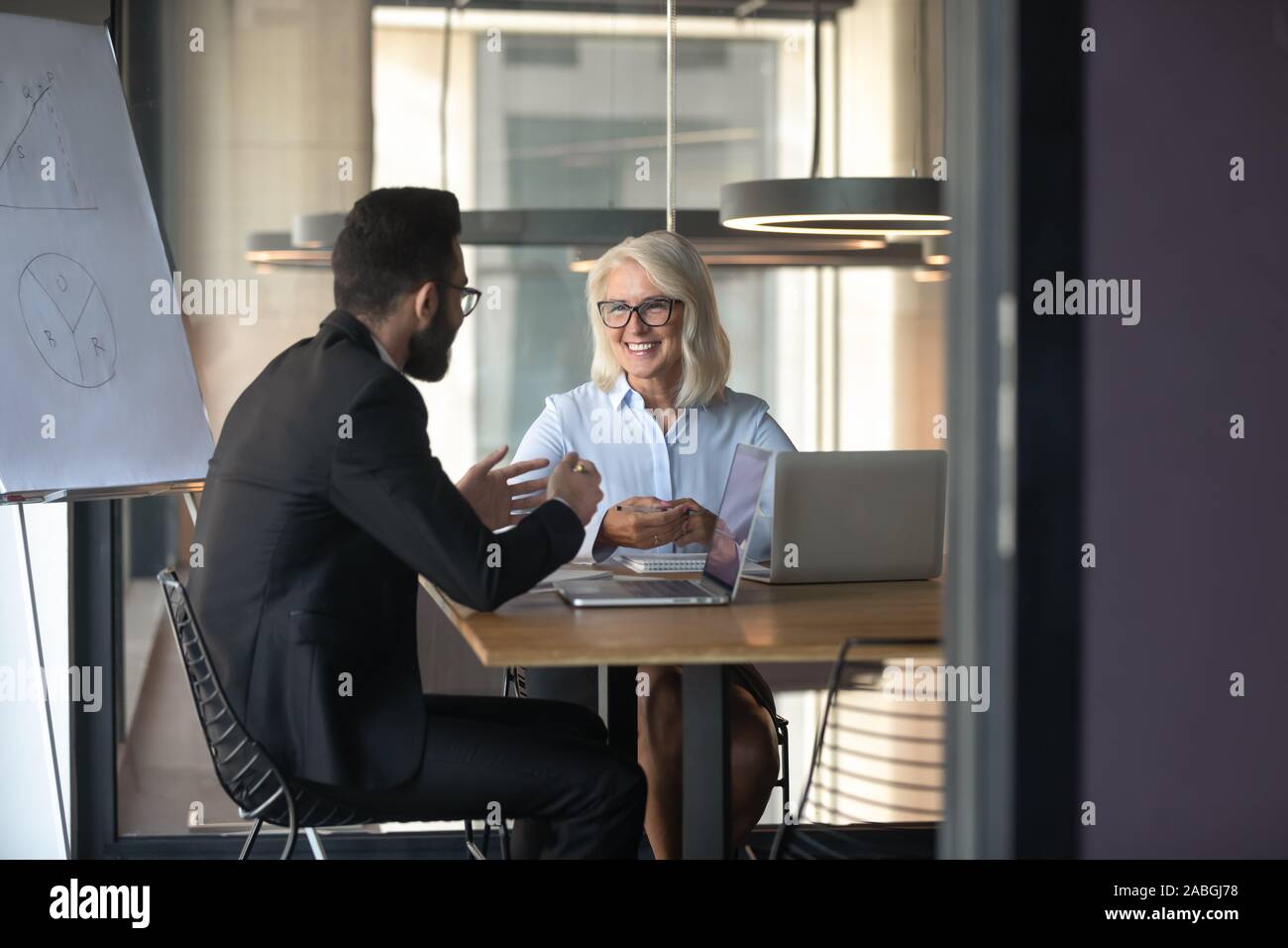 Diverse businesspeople smile talking at business meeting Stock Photo