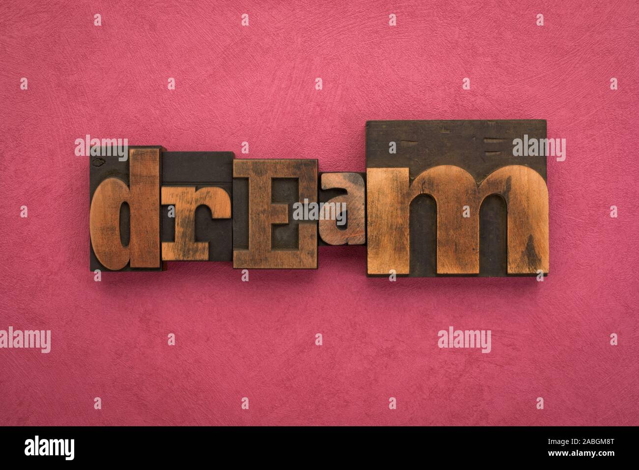 Dream, single word written with vintage letterpress printing blocks on textured pink background. Stock Photo