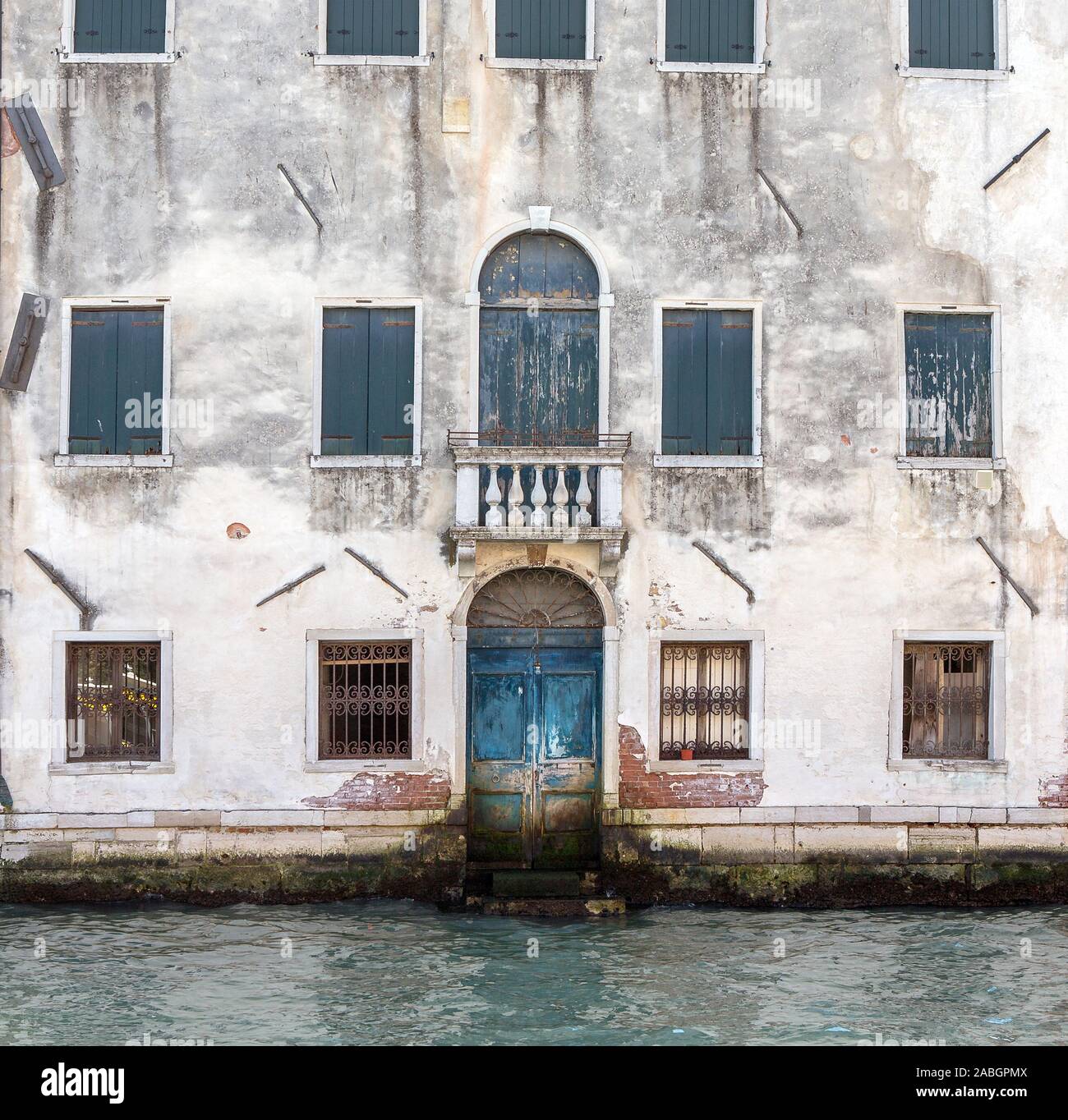 Partial view of old traditional abandoned building facing Grand Canal in Venice, Italy. Old bricks, windows, closed door, water. Stock Photo