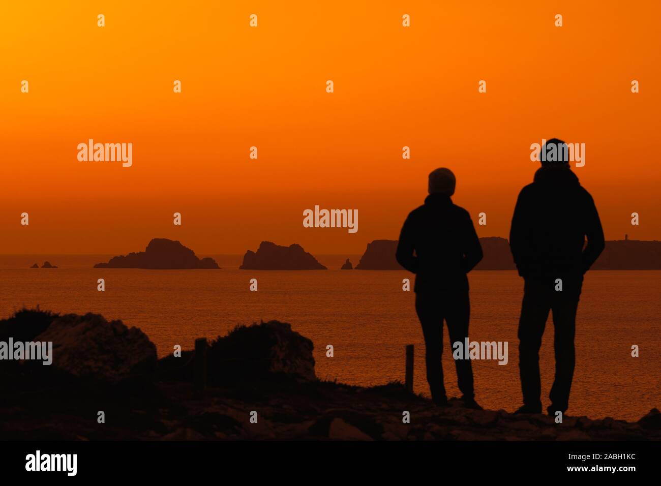 Couple watching sea cliffs at the Pointe de Pen-Hir and Les Tas de Pois sea stacks silhouetted against sunset, Crozon, Finistère, Brittany, France Stock Photo