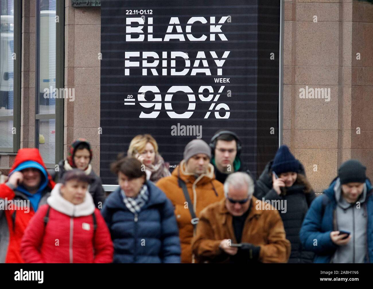 People walk passed a board with Black Friday sales discounts, outside a store. Black Friday is an informal name for the Friday following Thanksgiving Day in the United States which is celebrated on the fourth Thursday of November. The Black Friday is a sales offer to attract shoppers for the Christmas shopping season. Stock Photo