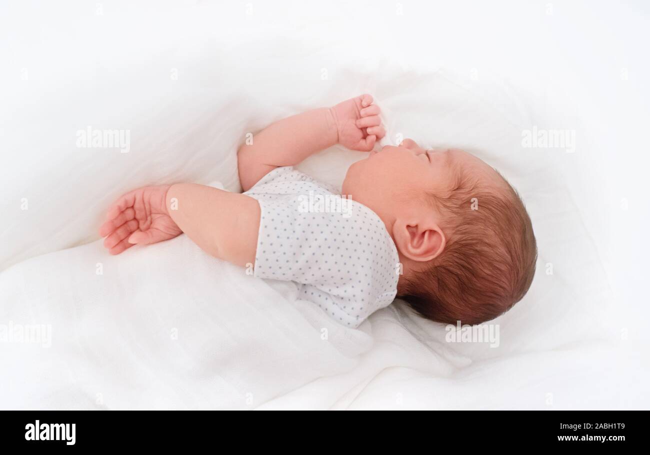 New born baby boy covering silk white bed sheet. Sleeping newborn baby