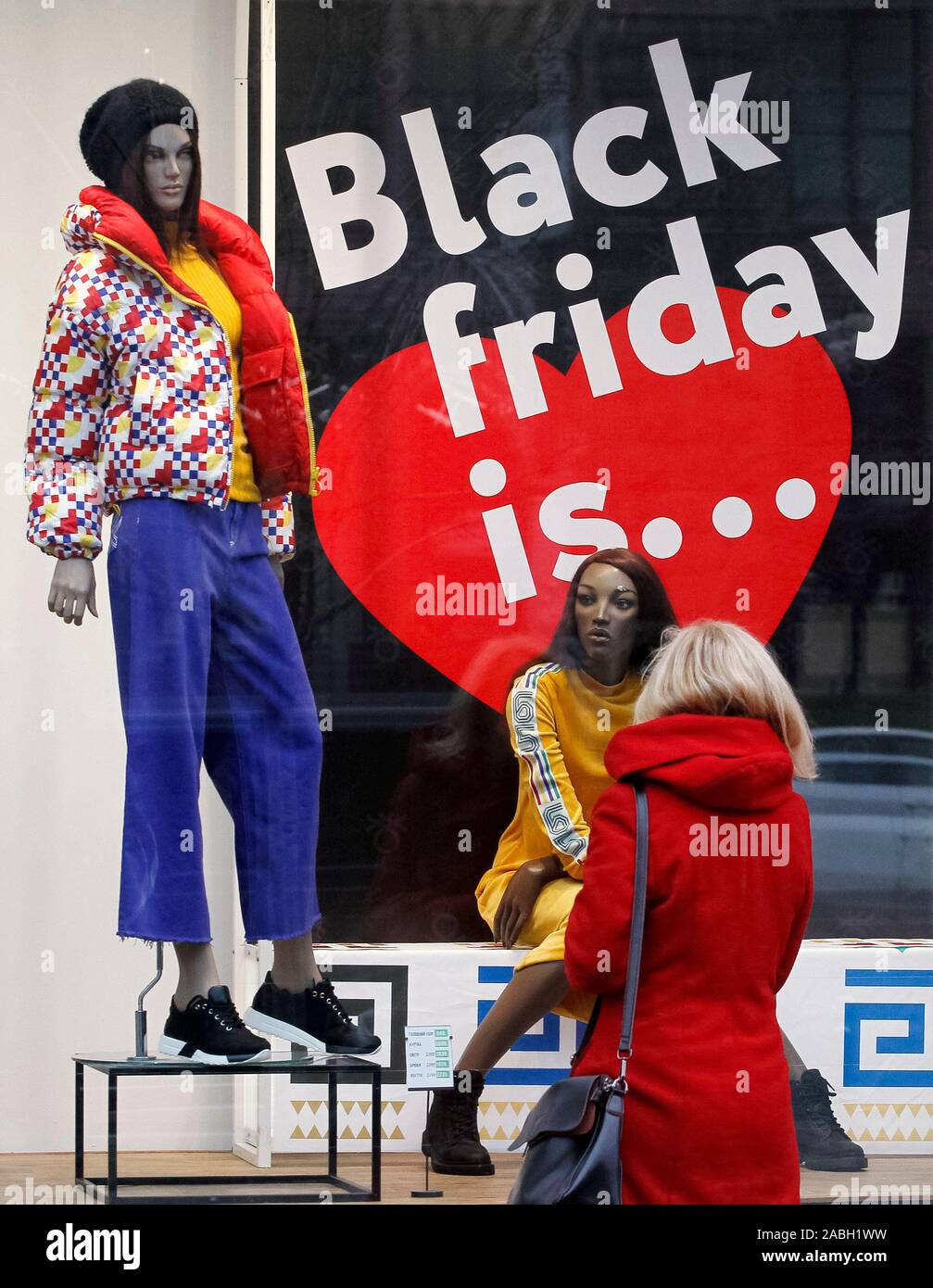 A woman looks at a board with Black Friday sales discounts, outside a store. Black Friday is an informal name for the Friday following Thanksgiving Day in the United States which is celebrated on the fourth Thursday of November. The Black Friday is a sales offer to attract shoppers for the Christmas shopping season. Stock Photo
