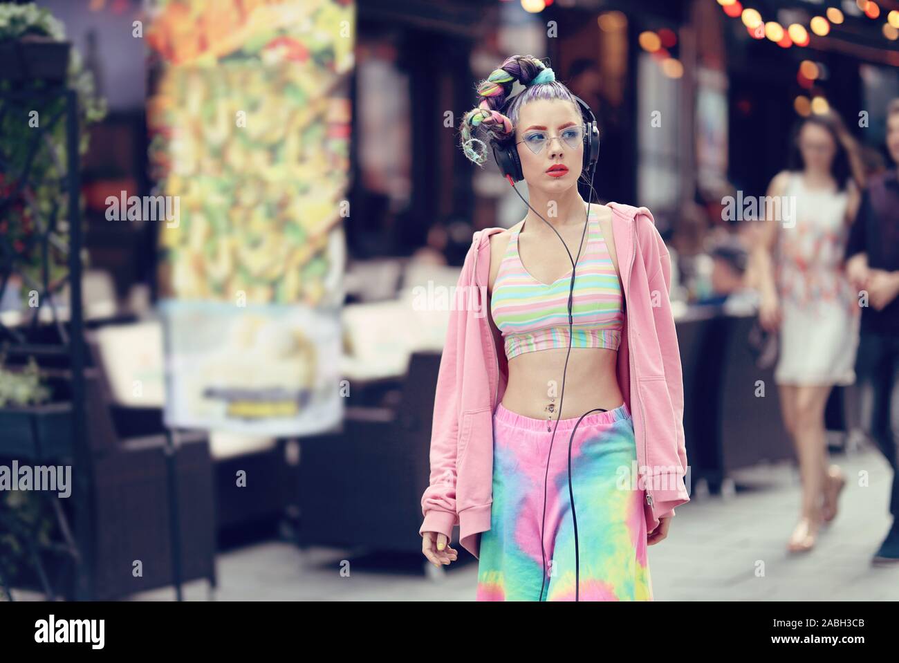 Modern fashion vanguard woman on the streets with trendy eyeglasses and piercings, listening music on headphones - Unique Avant-garde confident young Stock Photo