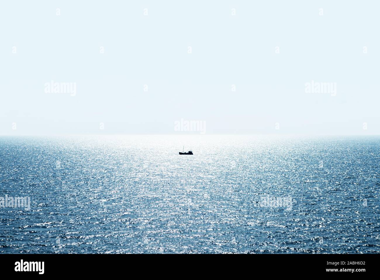 Lonely fishing ship trawler boat on ocean water. Calm clear sea sunny weather. Beautiful horizon of seascape Stock Photo