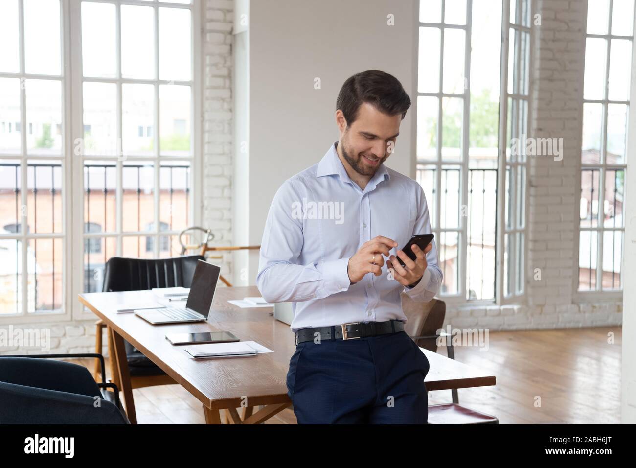 Smiling confident office manager using cellphone, enjoying break time. Stock Photo