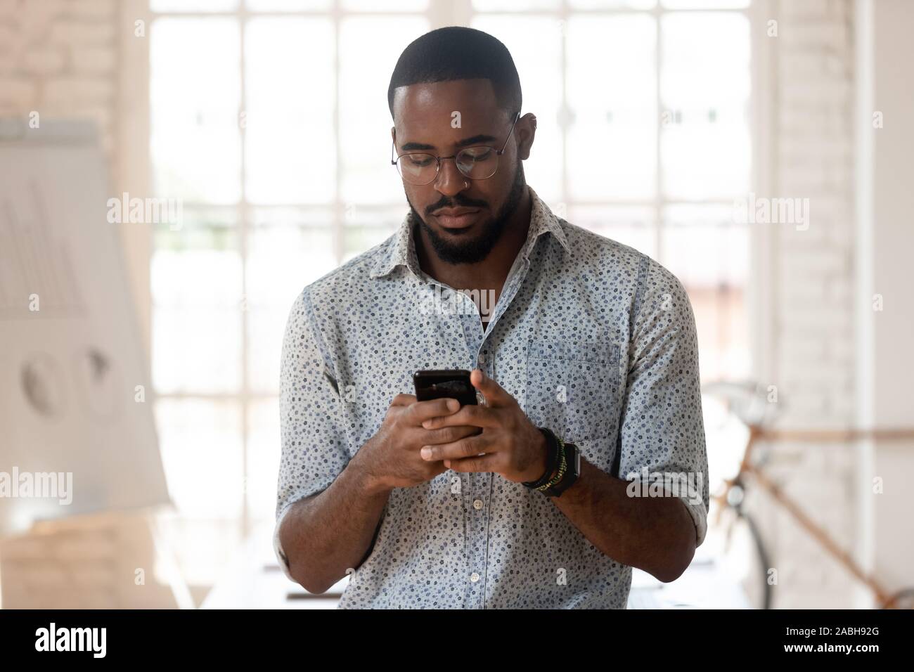 Serious african american young employee using smartphone. Stock Photo