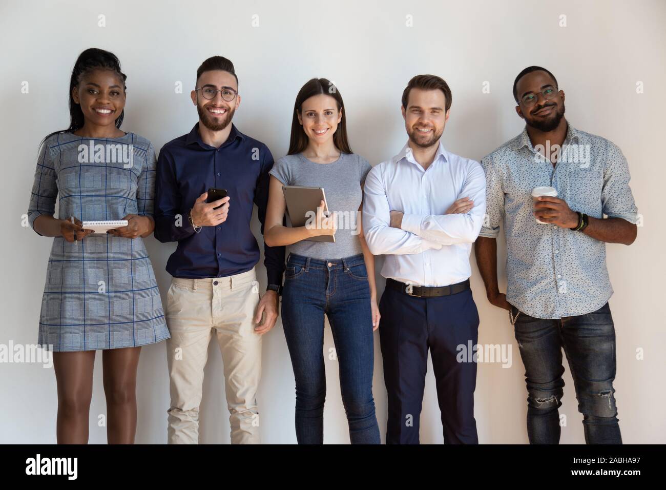 Happy confident successful multiethnic workers standing near wall. Stock Photo