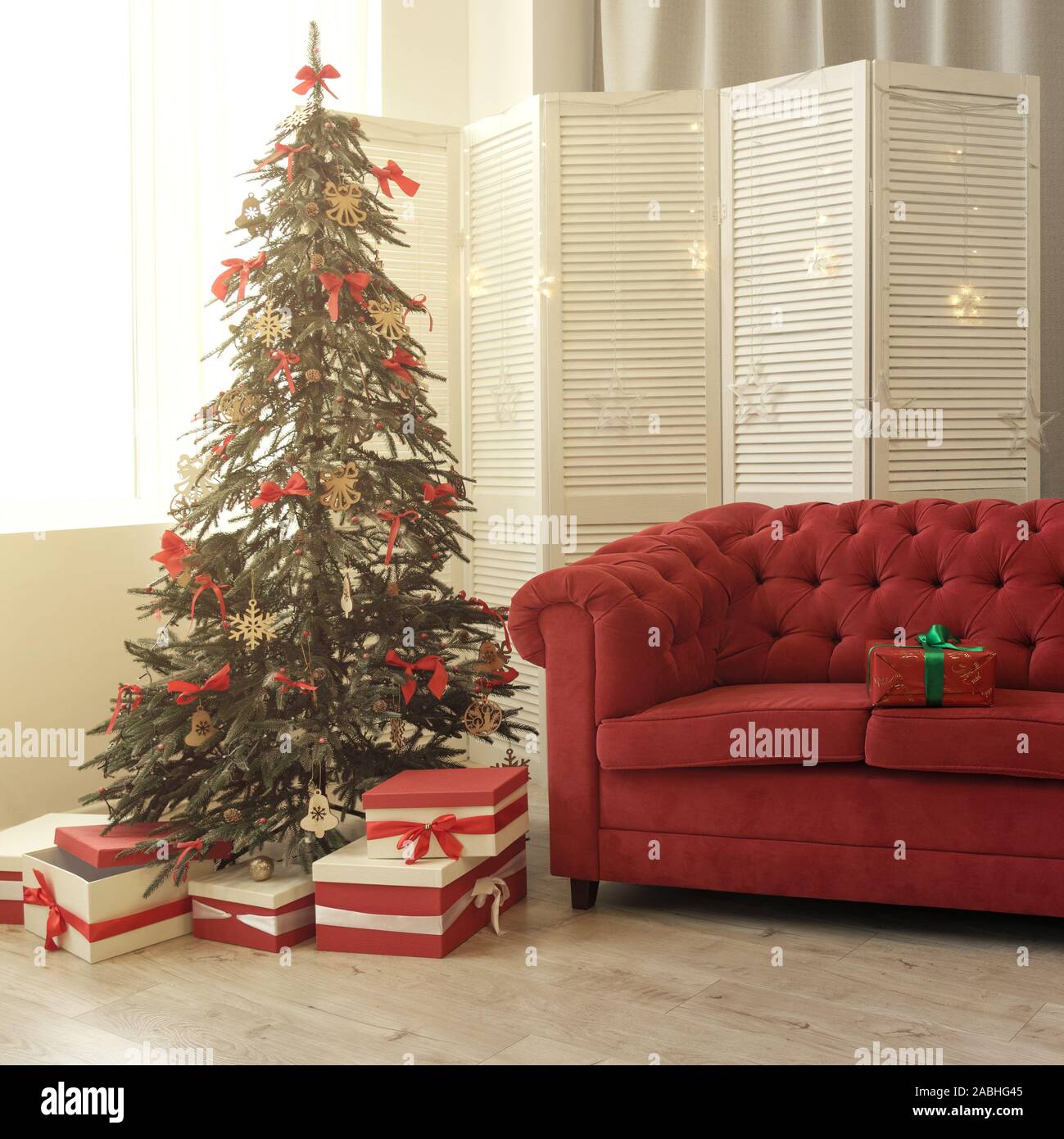 Gift Boxes Under Decorated Christmas Tree And Red Box On Red Sofa