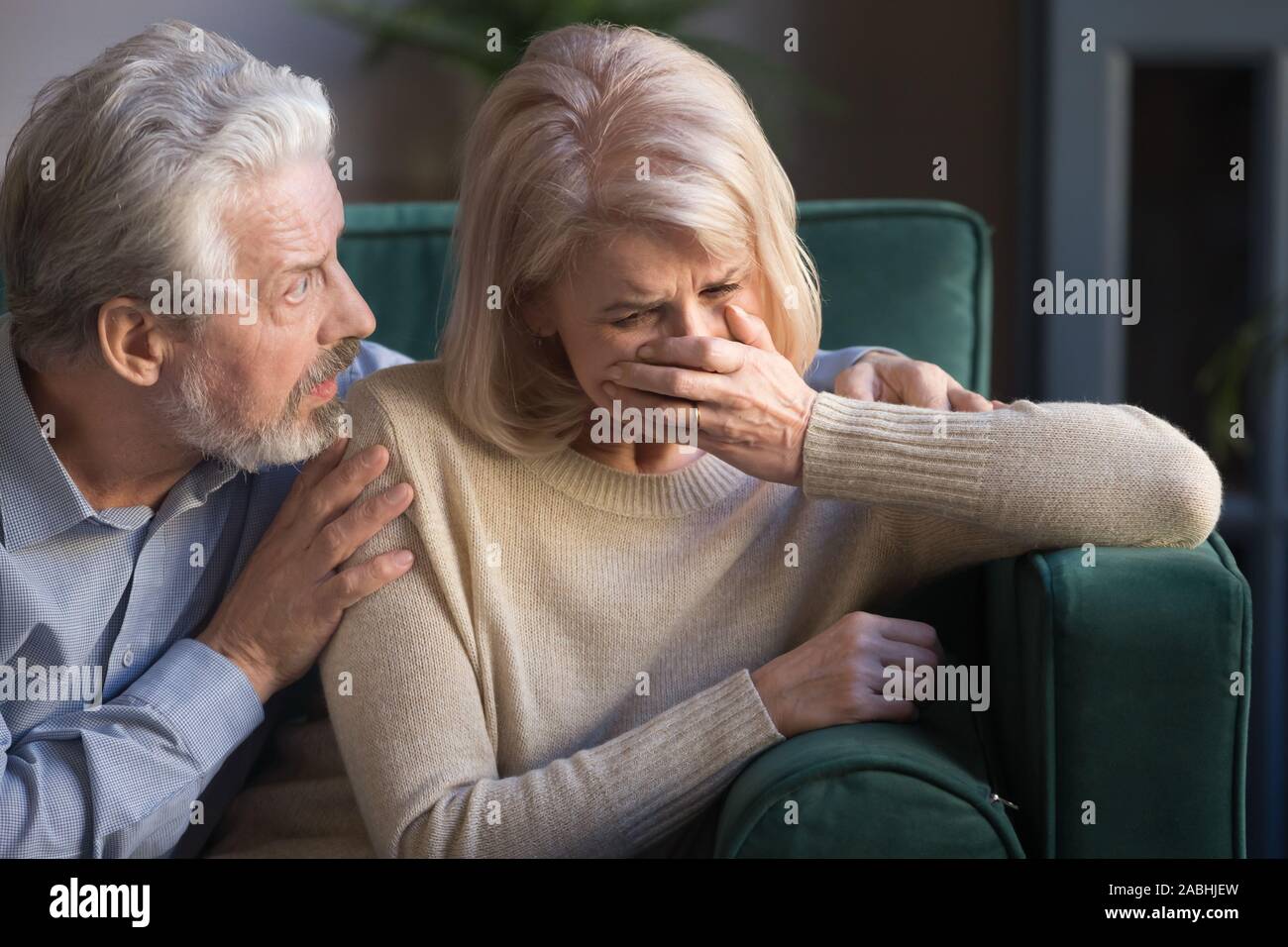 Elderly spouses indoors desperate wife crying worried husband comforting her Stock Photo