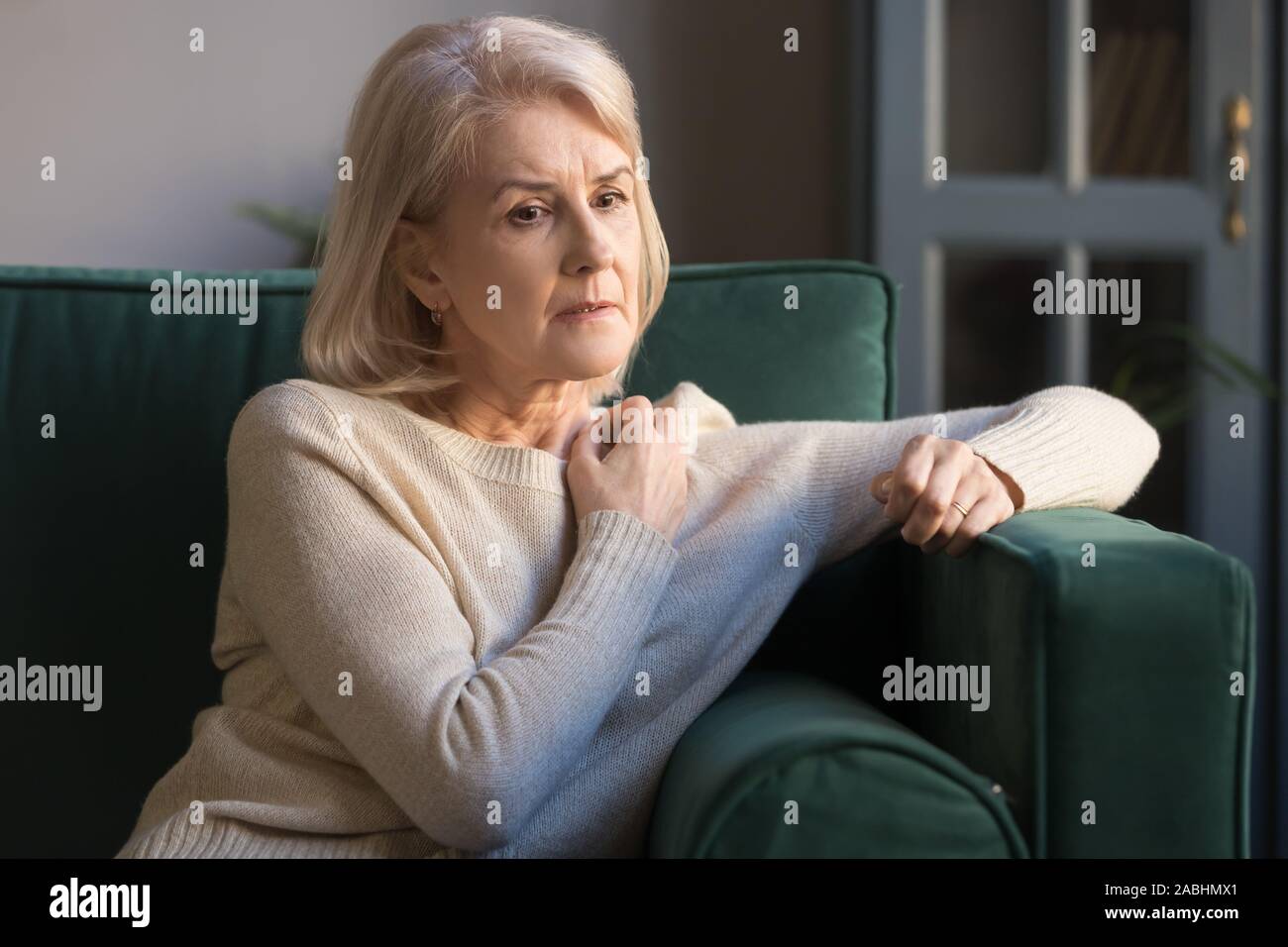 Mature depressed woman lost on thoughts sitting on couch Stock Photo